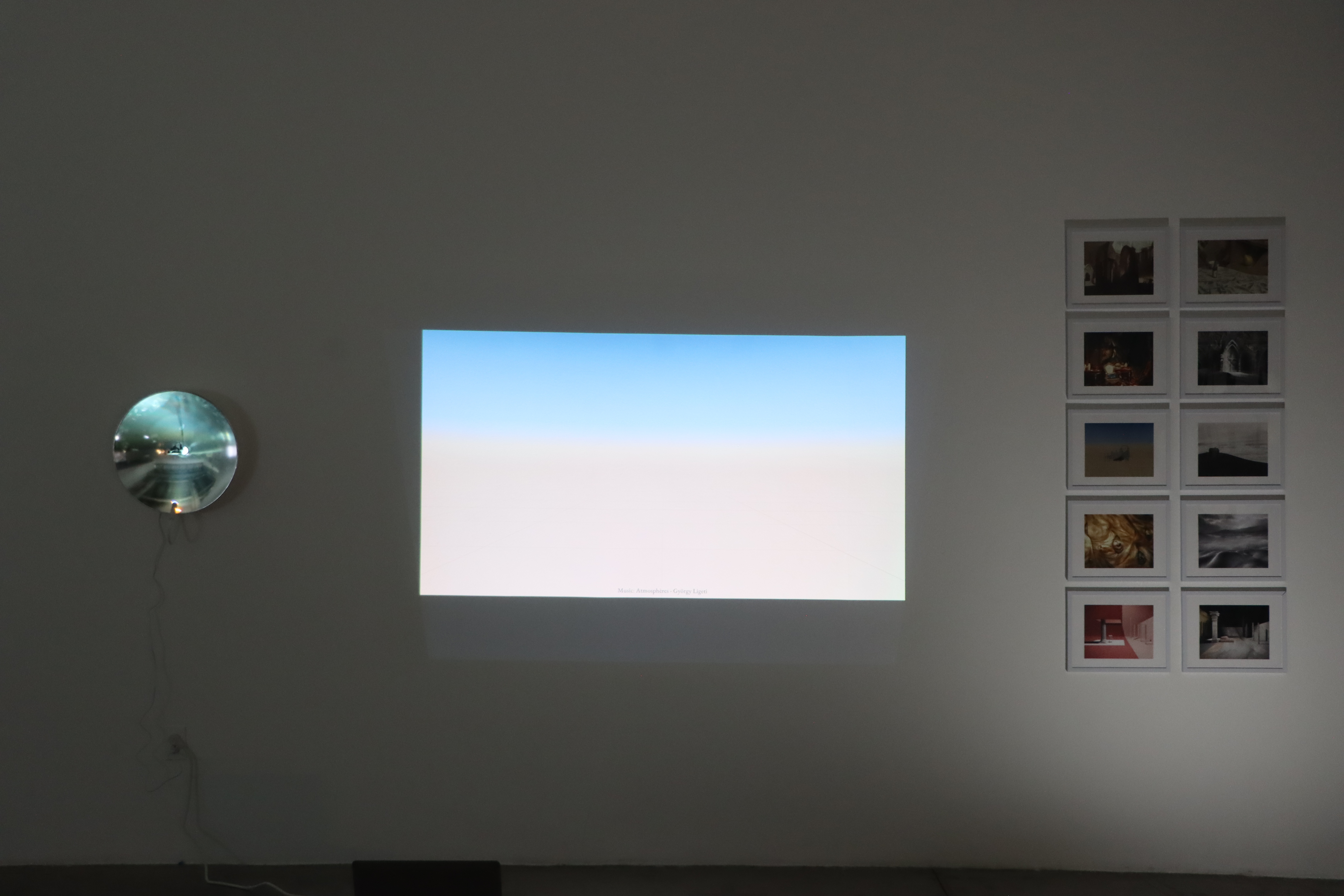 Gallery installation — convex mirror, video projection, and a grid of framed prints
