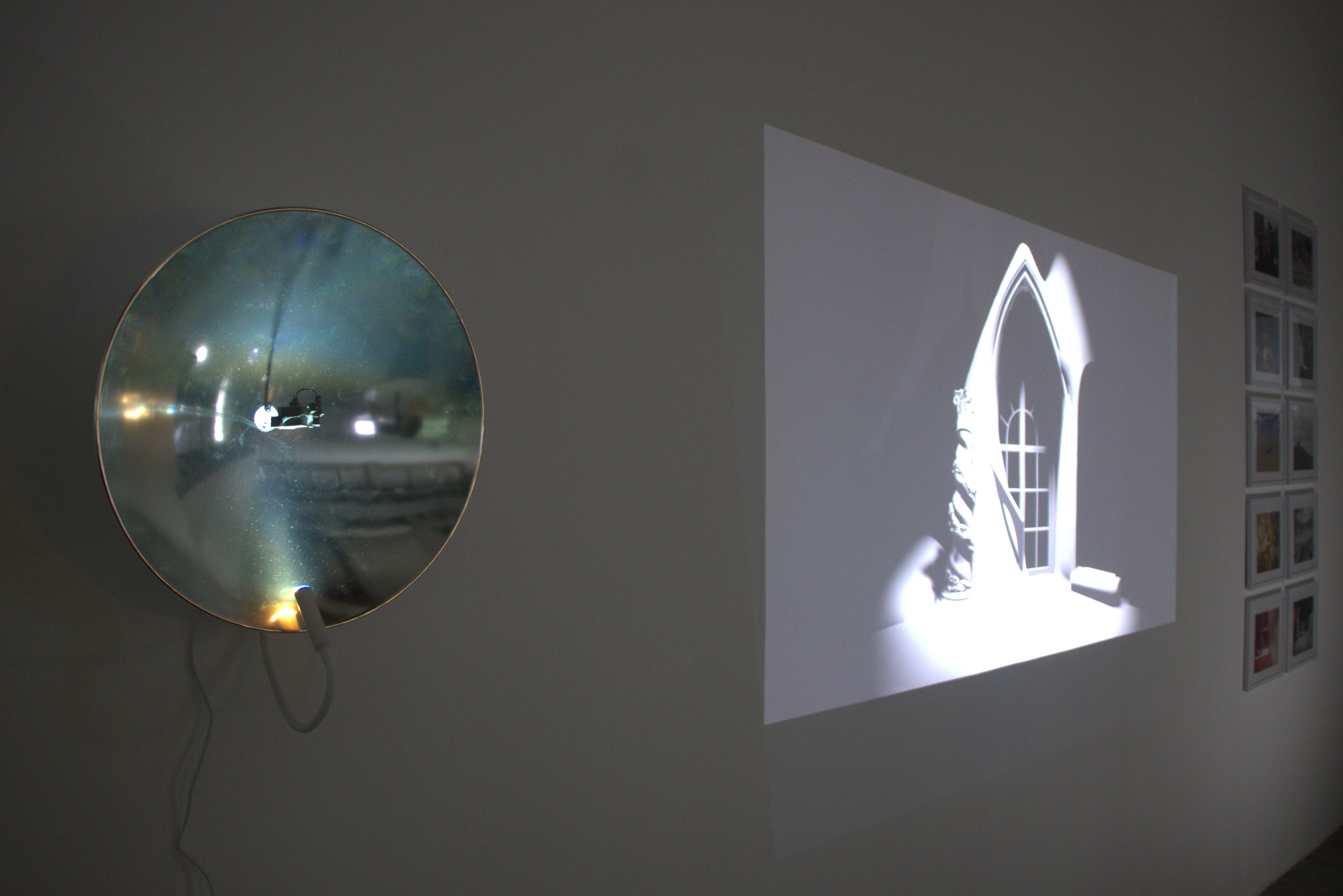 A gothic arched window projected onto the gallery wall, beside a convex mirror